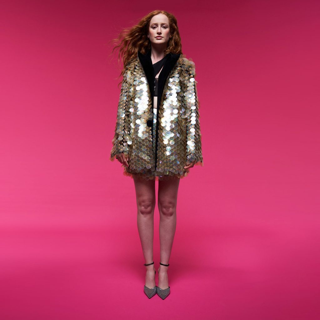 Oversized jacket made of large iridescent sequins with a one shoulder asymmetrical corset and a mini skirt made of iridescent large sequins.