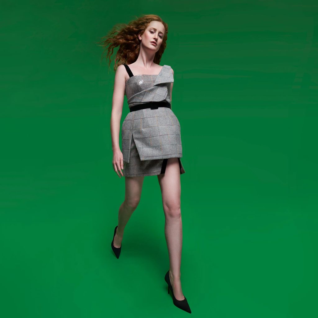 Short dress with asymmetrical shoulder straps and overlapping jacket flap bust, exaggerated waist and sequenced under skirt.
